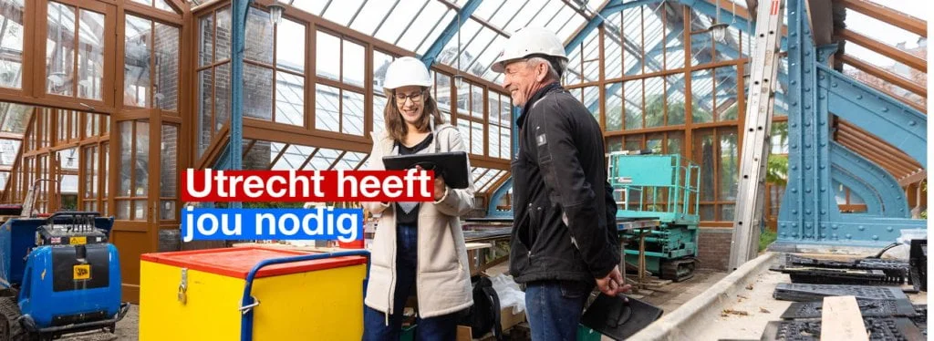 Twee mensen kijken op een tablet in een bouwloods. Tekst in beeld: Utrecht heeft jou nodig